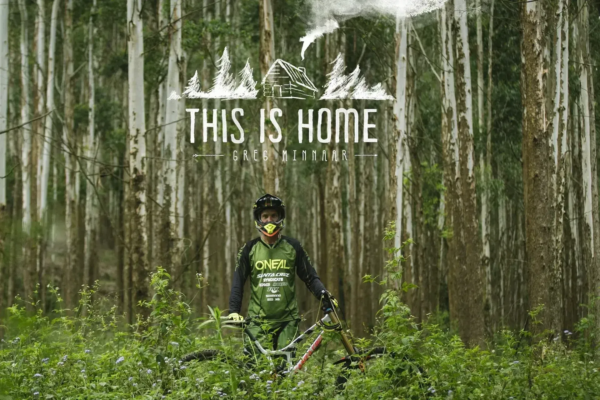 Official poster for  This is Home featuring mountain bike legend Greg Minnaar standing with his bike in a dense green forest beneath the film title.