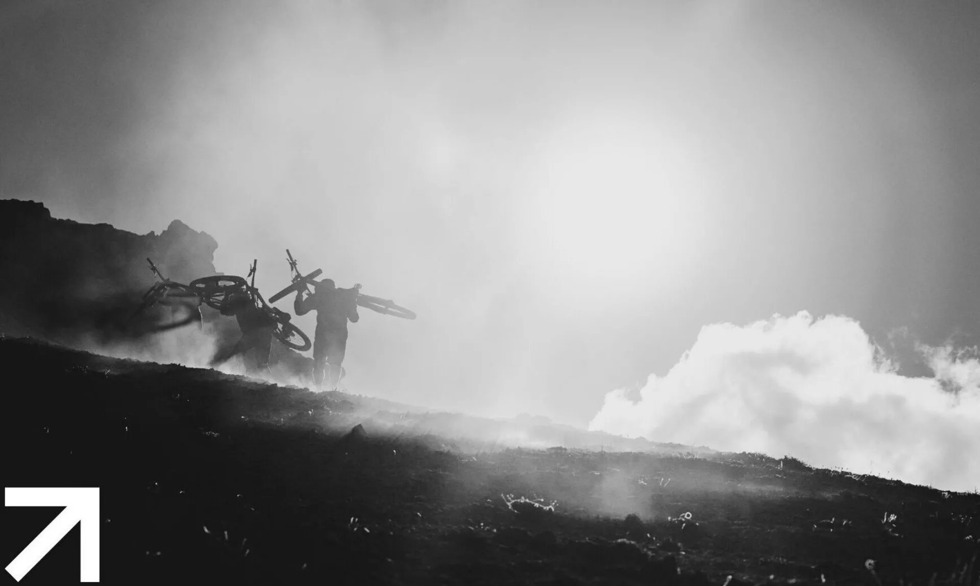 Mountain bikers hike up a ridge with bikes on their backs with UPRISING logo.